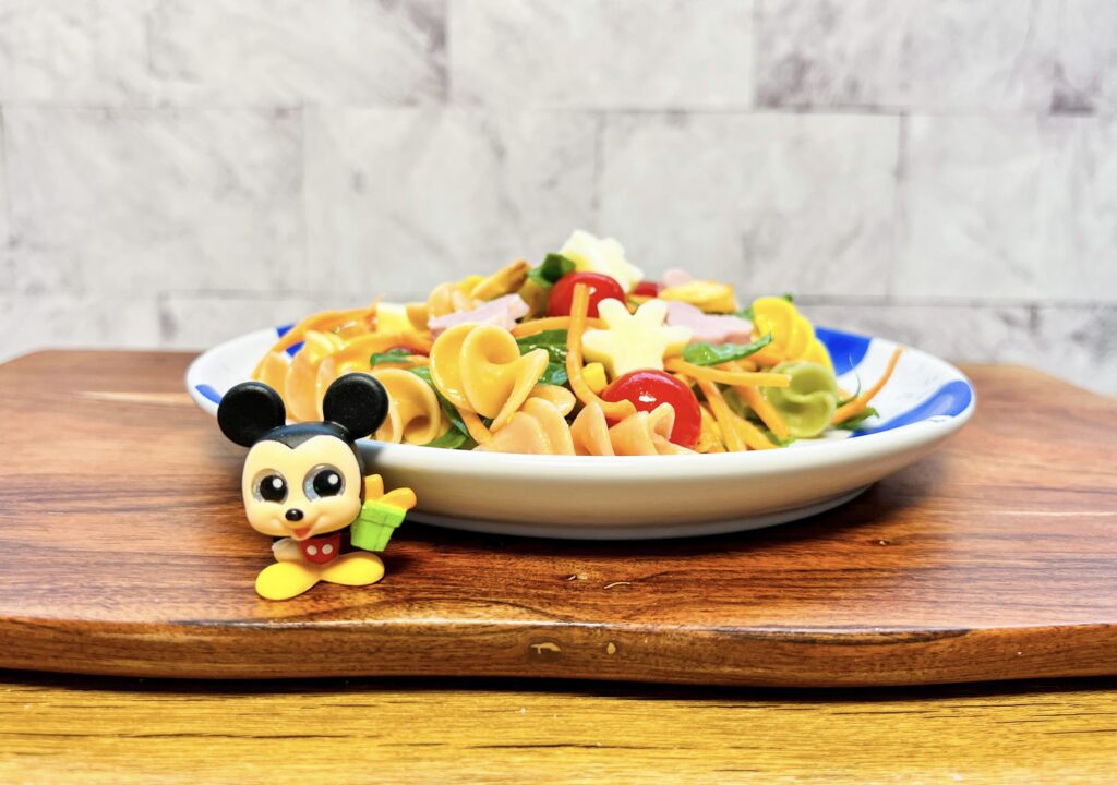 Ensalada de Pasta Colorida de Mickey Mouse hecha con pasta de colores, espinacas, jitomates cherry, zanahoria y granos de elite con jamón y crotones en forma de Mickey Mouse y queso mozzarella