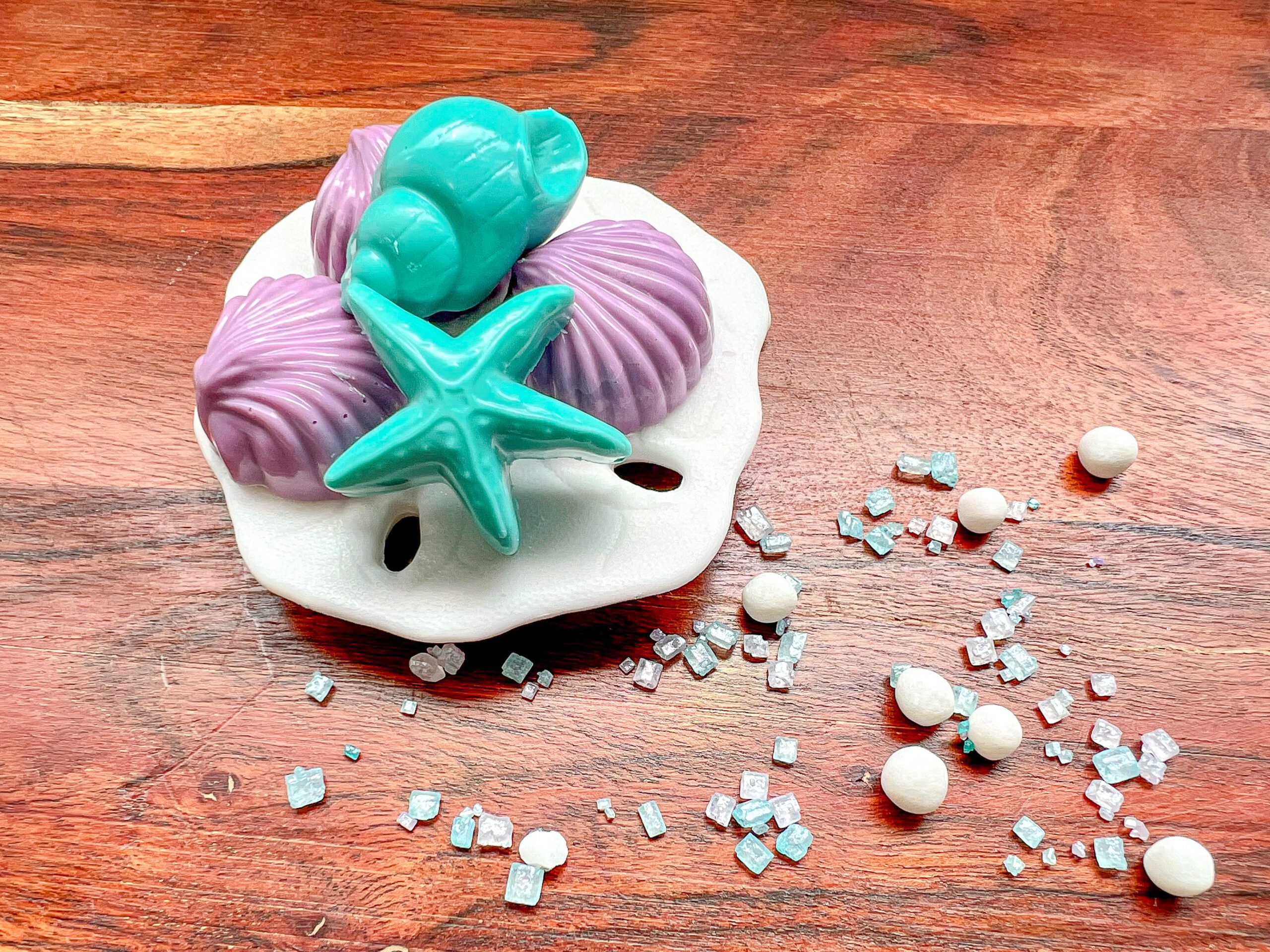 Imagen de tesoros dulces del océano representados con conchas marinas, estrellas de mar y caracoles hechos con caramelos para derretir de colores turquesa y morado.