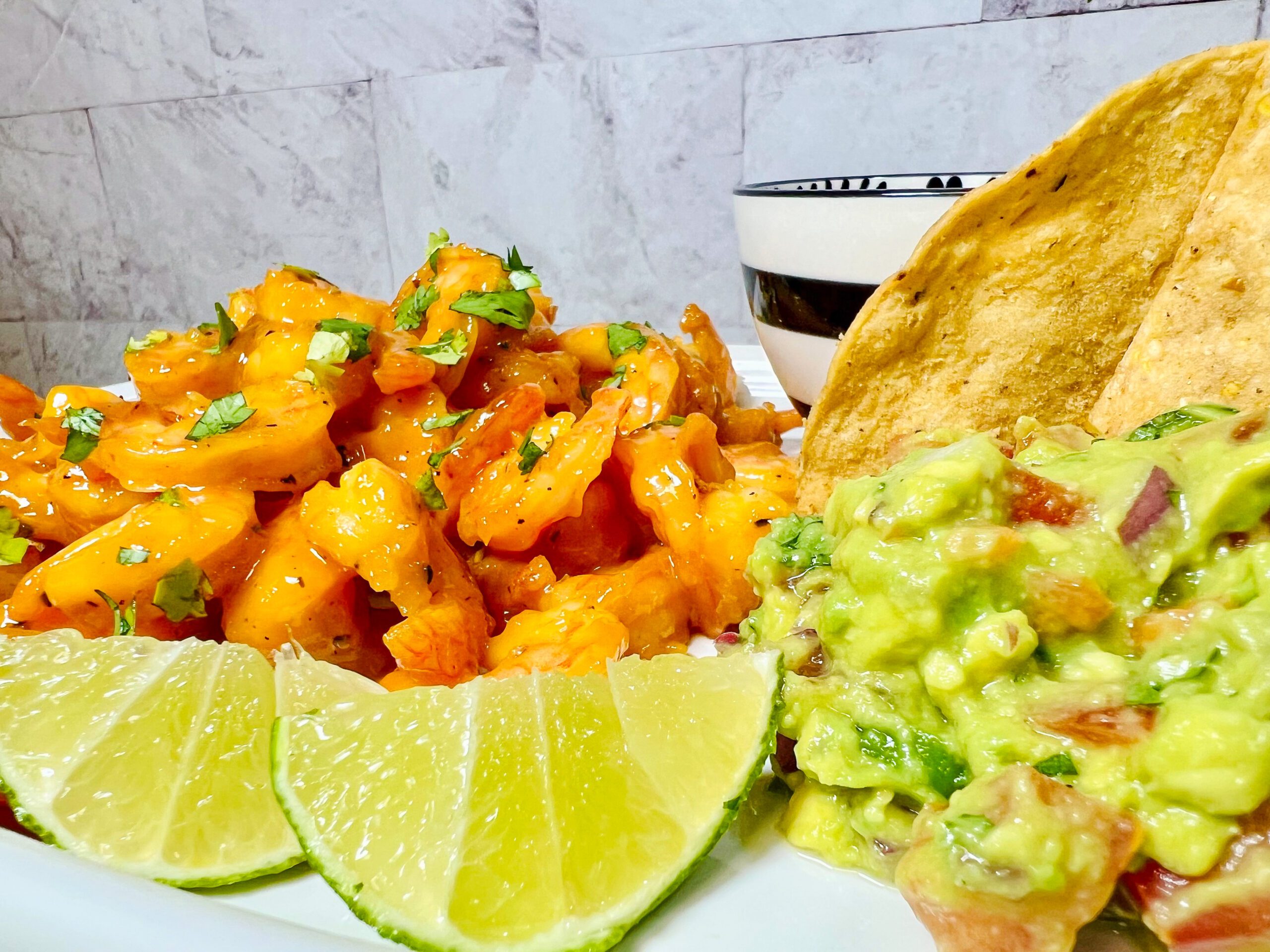 Imagen de un plato con camarones a la naranja servidos con guacamole y limón.