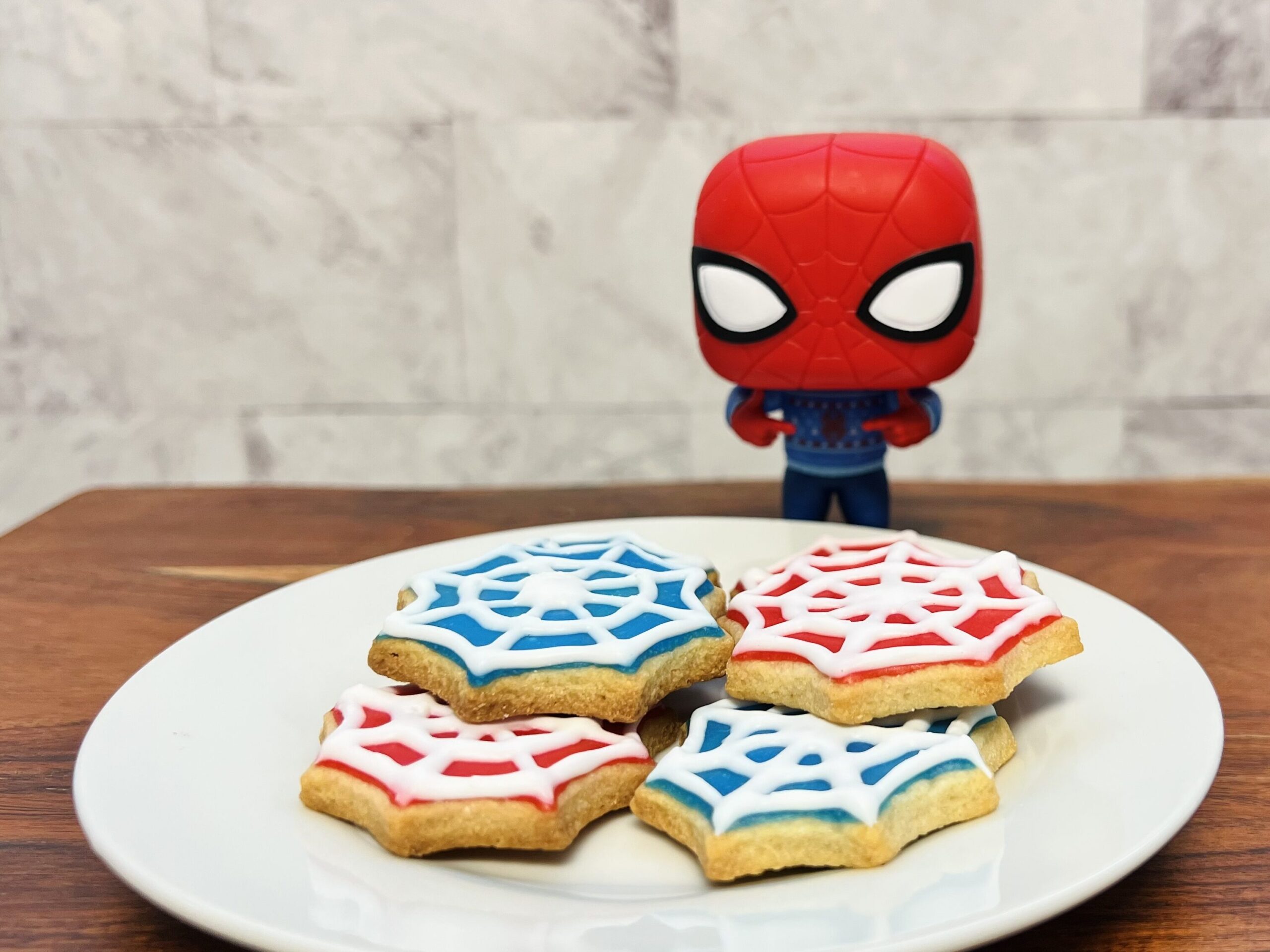 La imagen muestra un plato con galletas en forma de telaraña con glaseado rojo y azul.