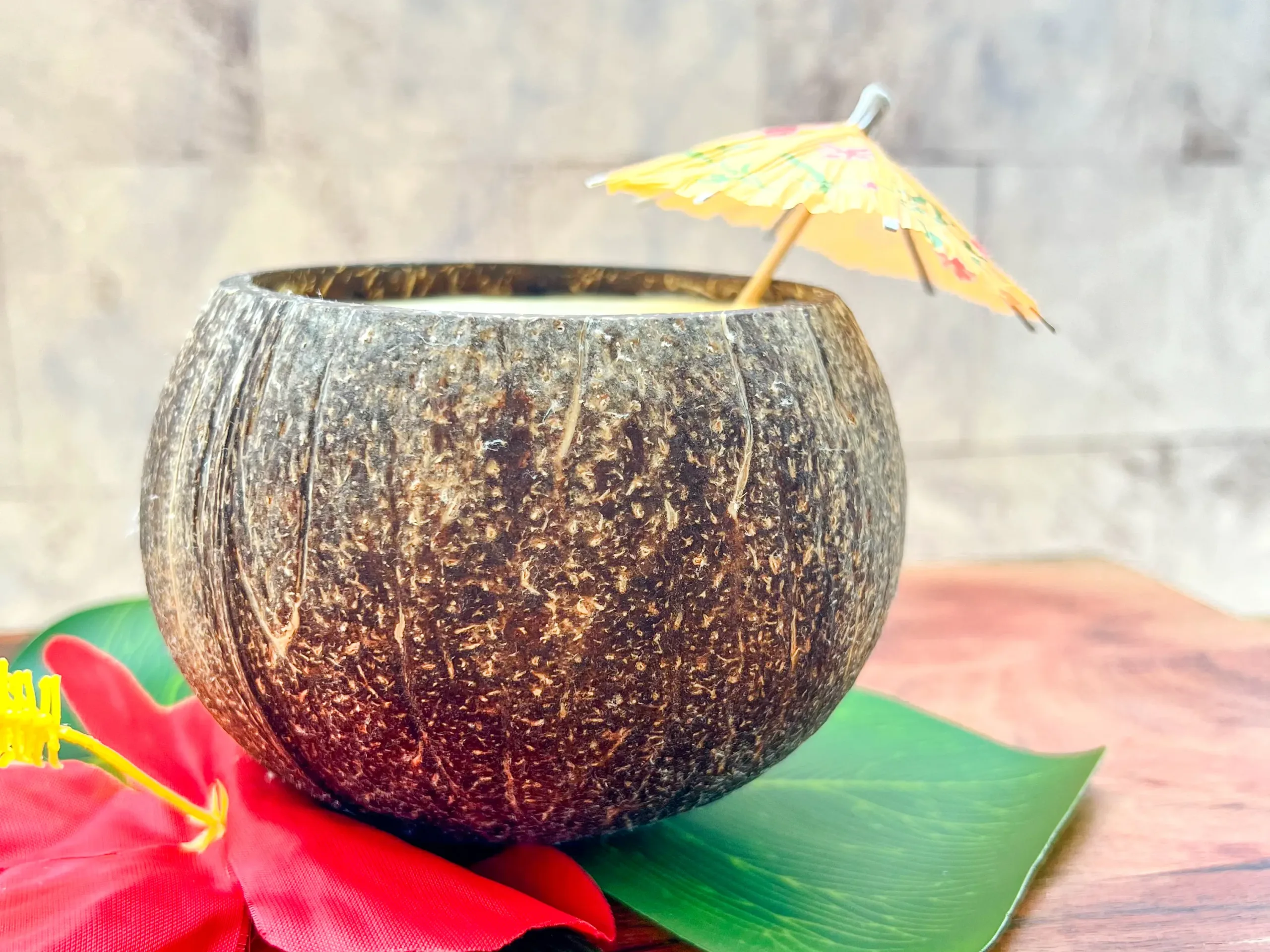 La imagen muestra un smoothie de mango-maracuyá servido en un coco con una sombrilla de papel como decoración.