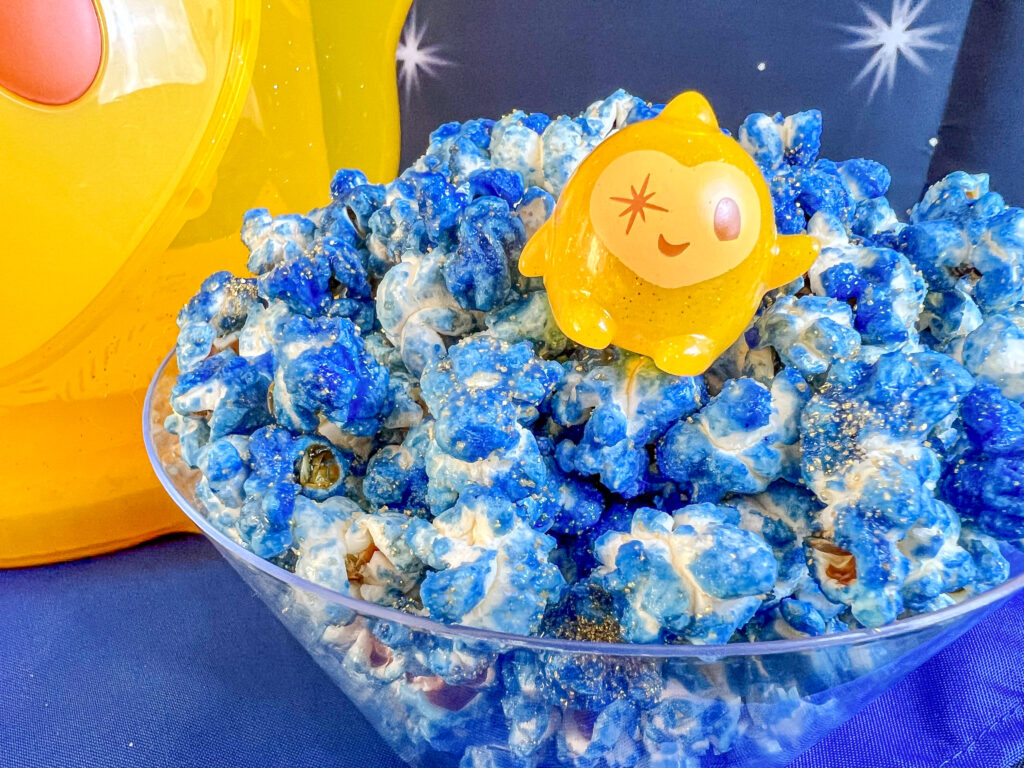 La imagen muestra un recubiente con palomitas azules con destellos dorados inspiradas en la película de Disney “Wish”
