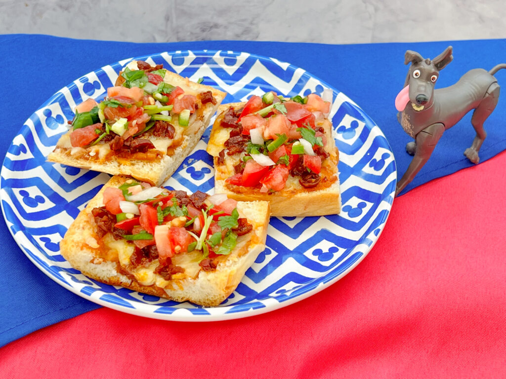 La imagen muestra 3 molletes de chorizo con pico de gallo sobre un plato blanco con azul.