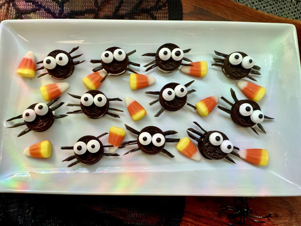 La imagen muestra unas mini arañas de oreo y patas de dulce de regaliz con ojos comestibles. Las arañas están servidas en un plato rectangular con dulces de maíz 